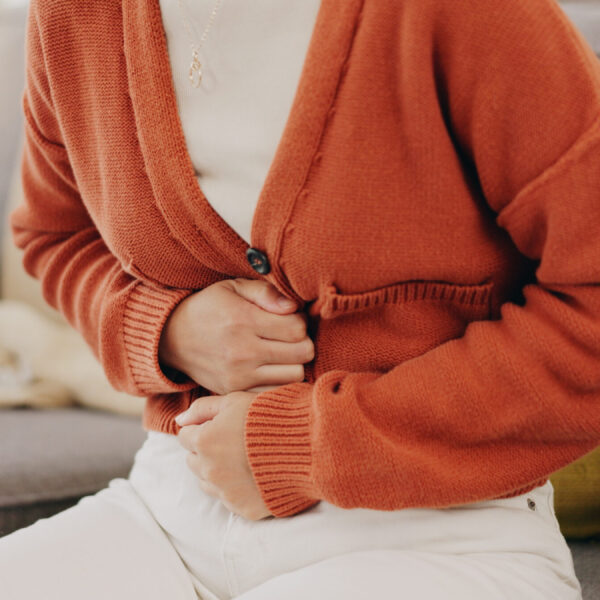 Stomach ache, cramps and hands of woman with abdomen pain due to constipation, menstruation or ibs issue. Sick, home and person suffering and holding belly in a house lounge, couch and living room.